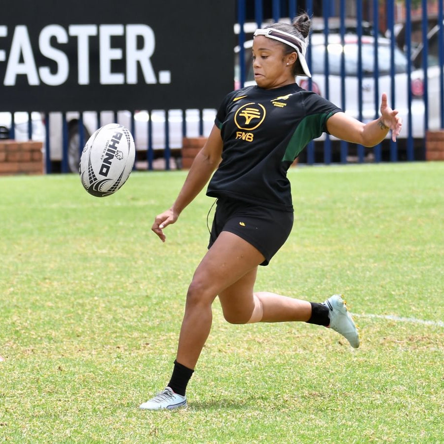 Alicia Willemse mid kicking a 'Rhino' Rugby ball at Springbok Women's training on a grassy pitch