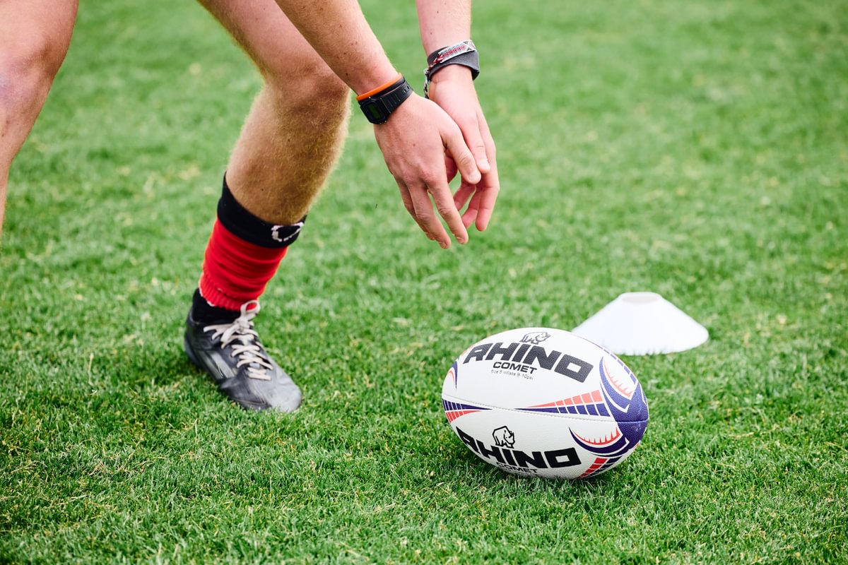 Person preparing to kick a Rhino branded rugby ball on grass