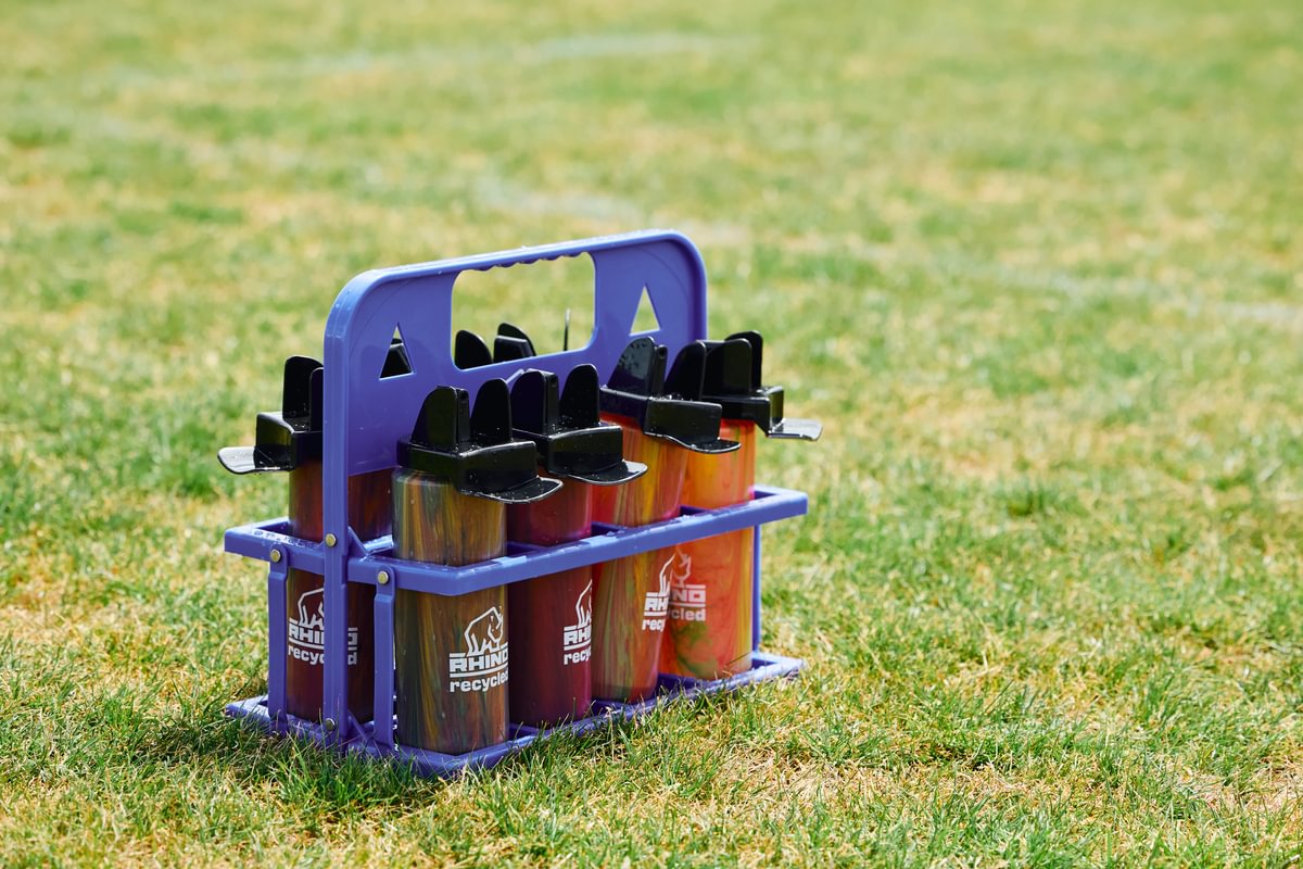 Orange marbled colour water bottles in a blue carrier with 'Rhino Recycled' branding on a grassy rugby pitch