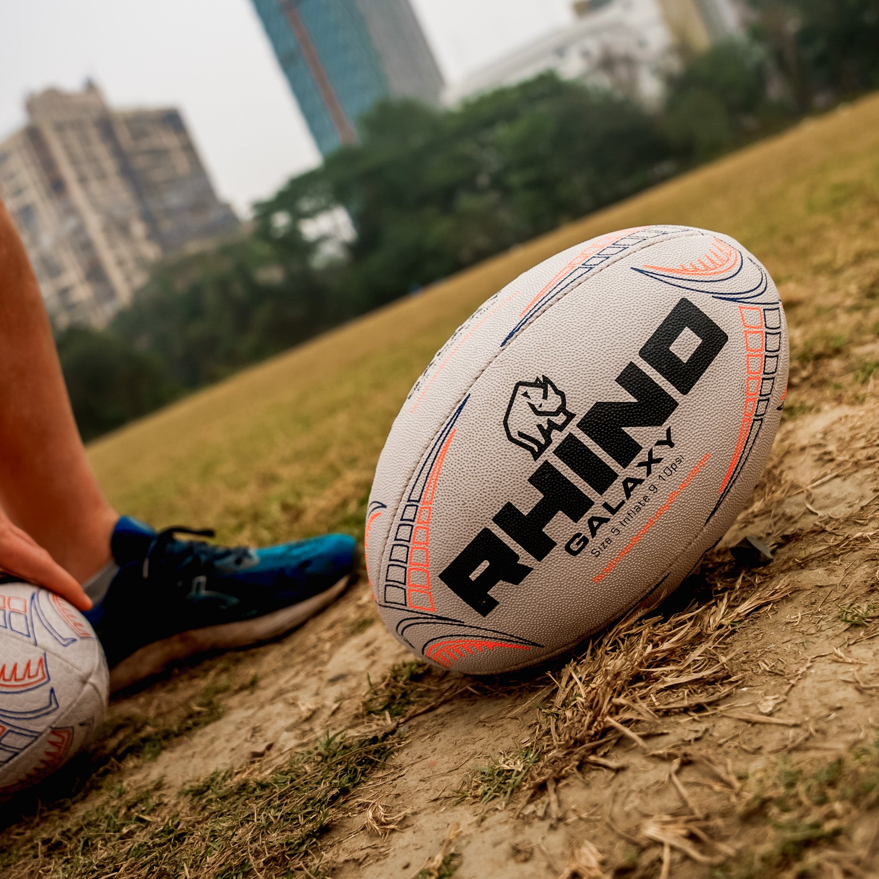 Rhino Galaxy rugby ball on a grassy field with blurred cityscape in the background