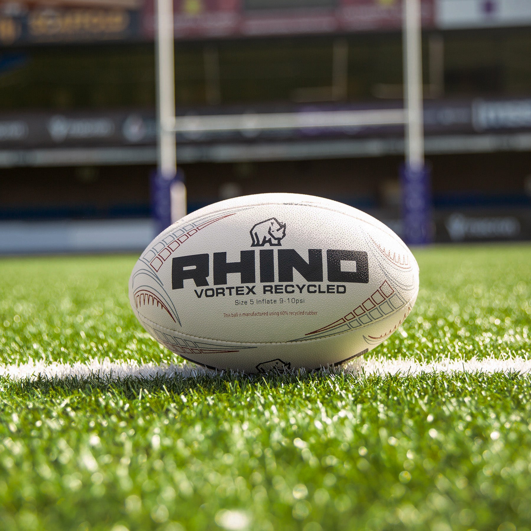 Rhino branded rugby ball on a grass field with stadium in the background