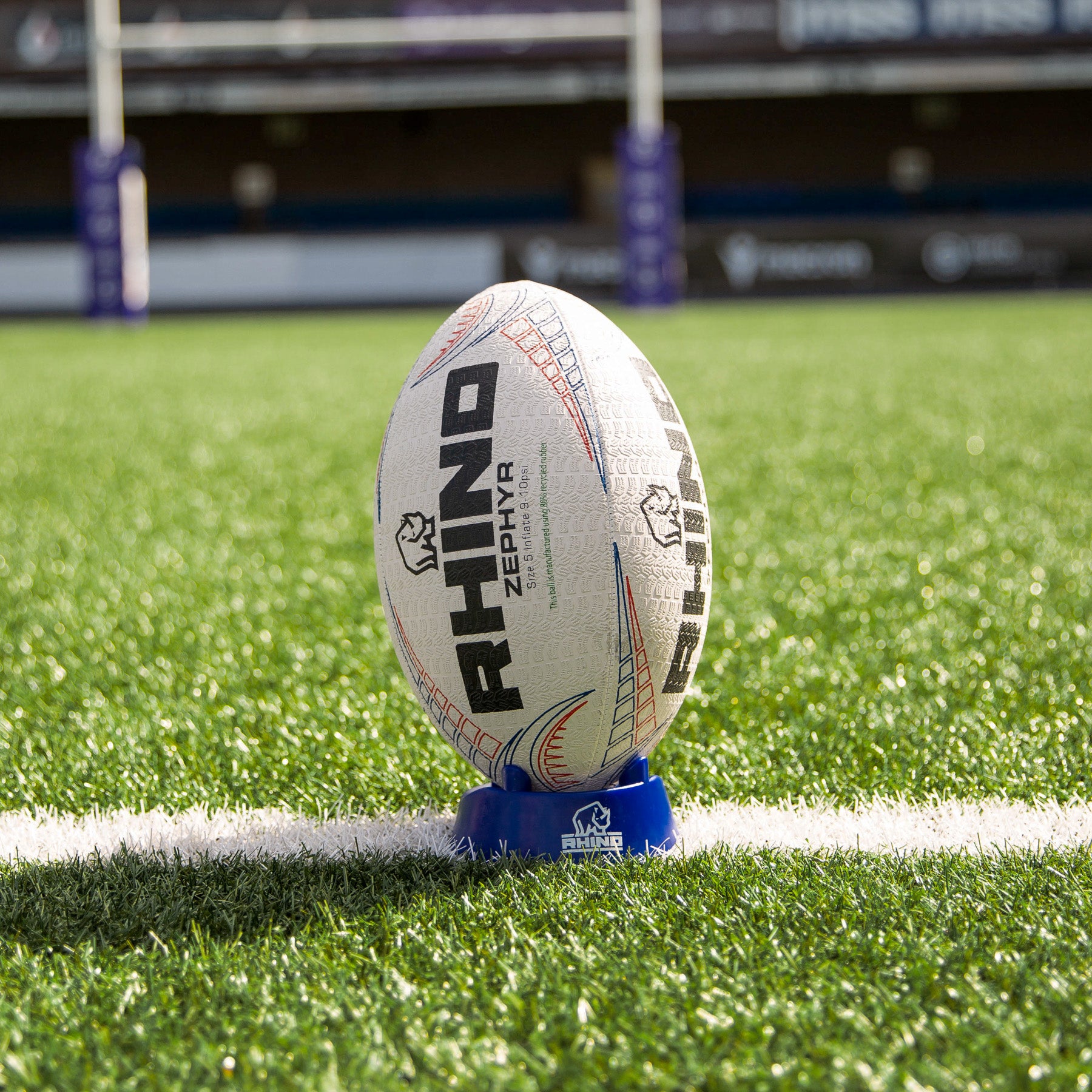Rugby ball on a blue kicking tee with 'Rhino' branding on a grass field