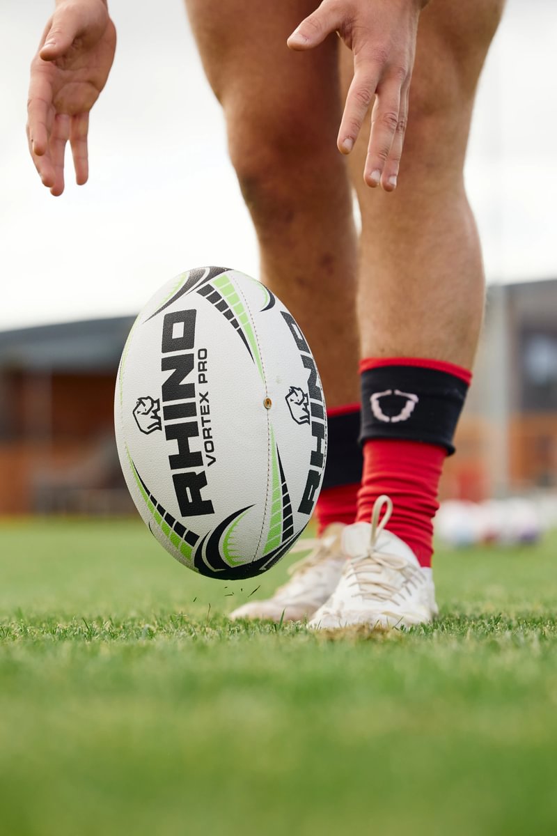 Person preparing to kick a Rhino branded rugby ball on a grass field