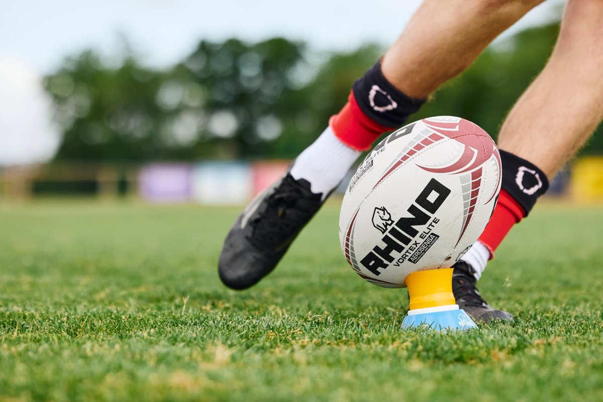 Person preparing to kick a Rhino branded rugby ball on a grass field