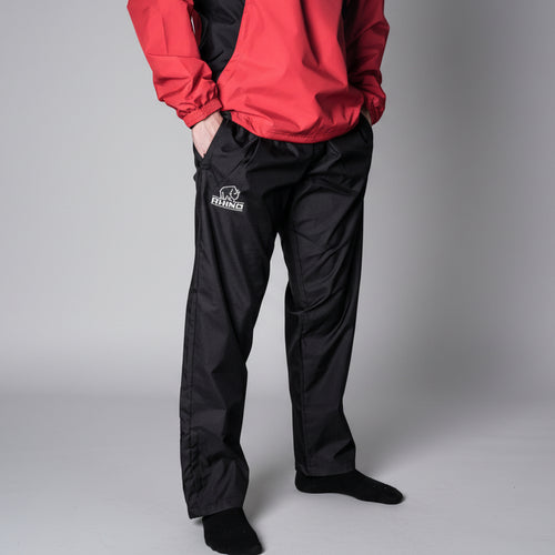 Person wearing a red jacket and black pants with a Rhino Rugby logo on a gray background